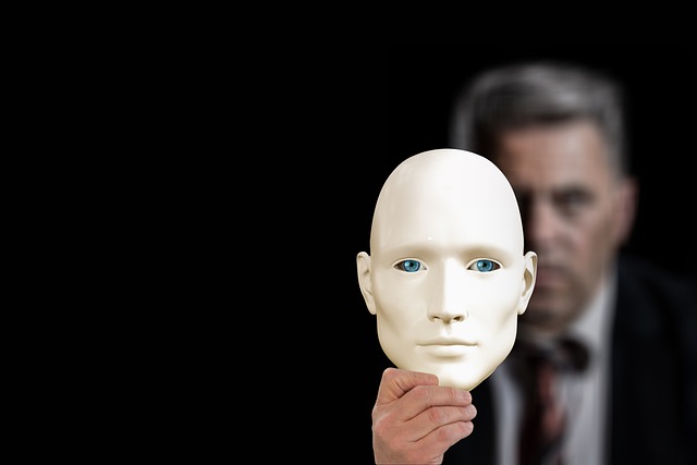 An individual holding a white mask with a neutral expression in front of their face, symbolizing hidden identity or deception, with a blurred figure in the background, representing mystery or manipulation.